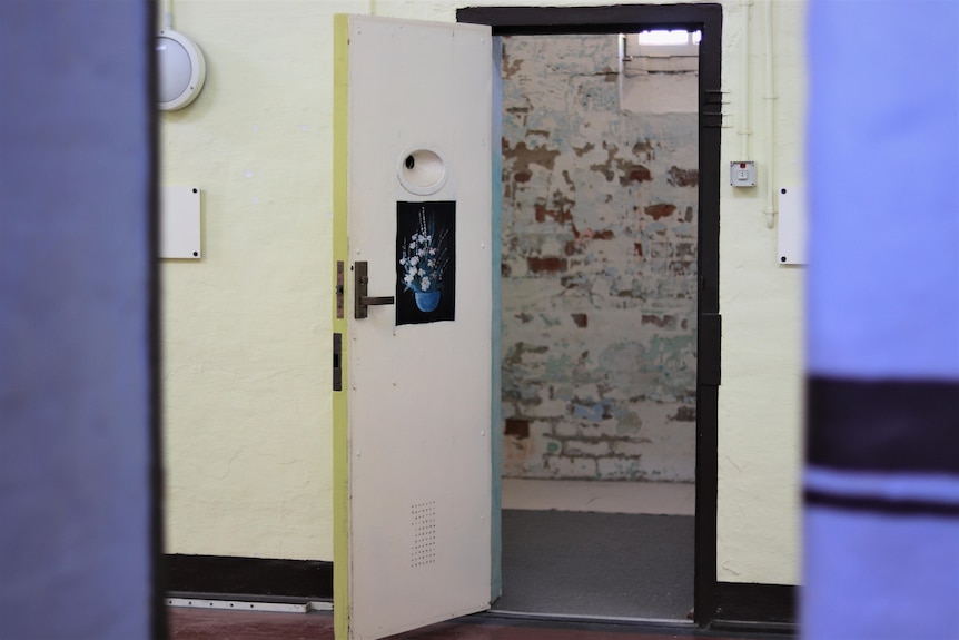 A prison cell with an open door and a piece of art stuck on it. 