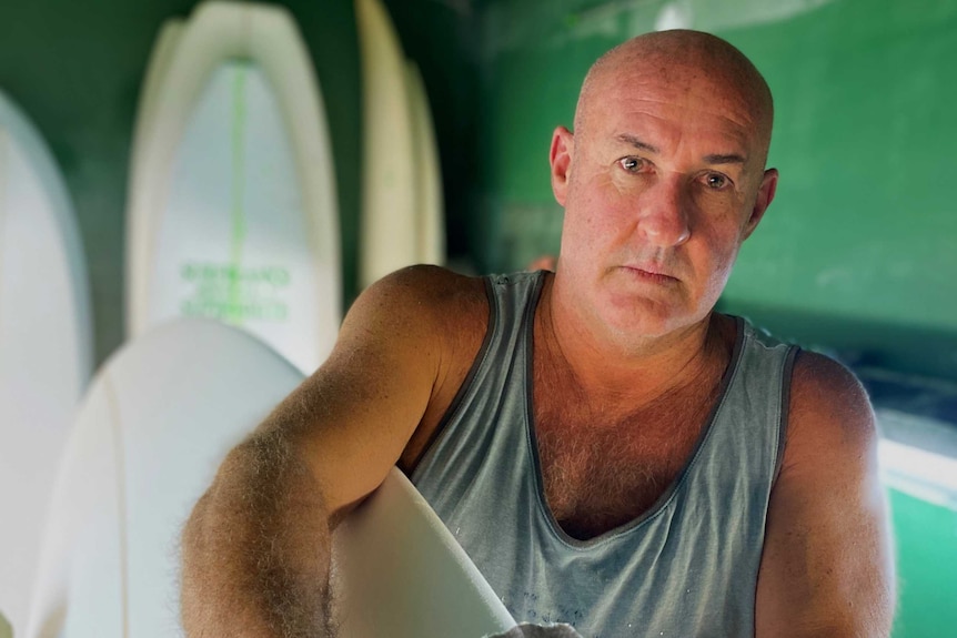 A man holds a surfboard while looking into the camera.