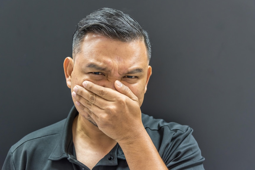 Close-up photo of man covering his nose and face with his hand and screwing up his face as if smelling something terrible.