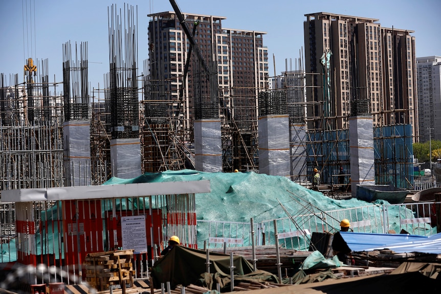 Workers wearing yellow hard hats at a construction site with lots of tall upright steel beams.