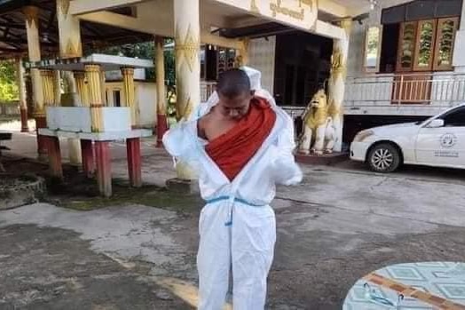 A monk putting on a PPE suit over his robes. 