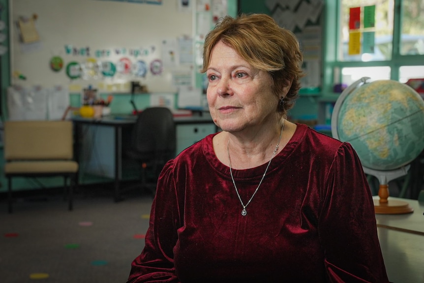 A woman sits in a classroom, looking to the left of the camera.