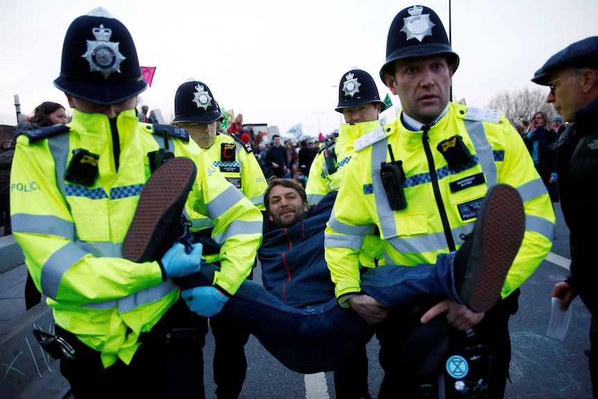 Four police officers carry a man by his arms and legs.