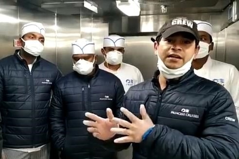 A man in a facemask standing in a kitchen in front of four other men in chef's uniforms and masks