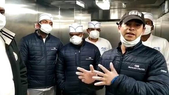 A man in a facemask standing in a kitchen in front of four other men in chef's uniforms and masks