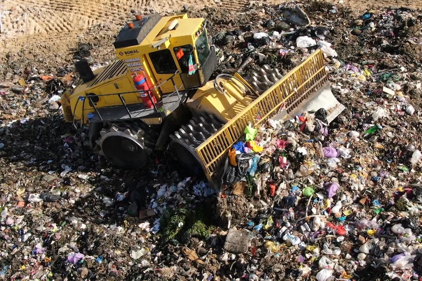 An aerial photograph of rubbish being bulldozed into a pile in landfill.