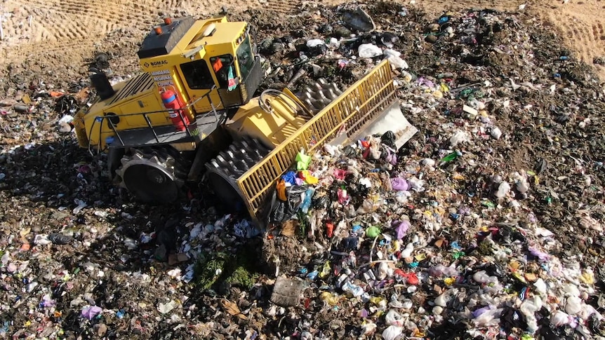 An aerial photograph of rubbish being bulldozed into a pile in landfill.