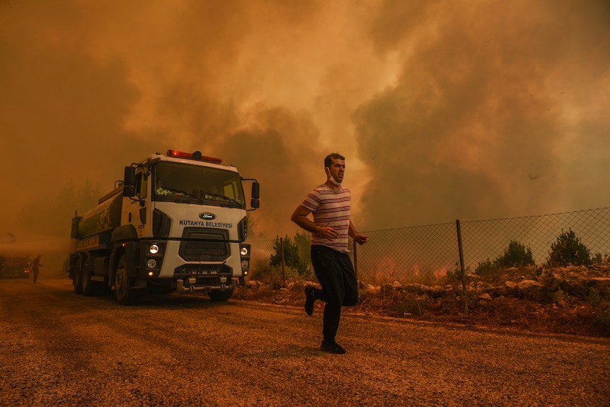 一名男子在街上奔跑逃离火灾，在火灾后可以看到一辆消防车和充满烟雾的橙色地平线。