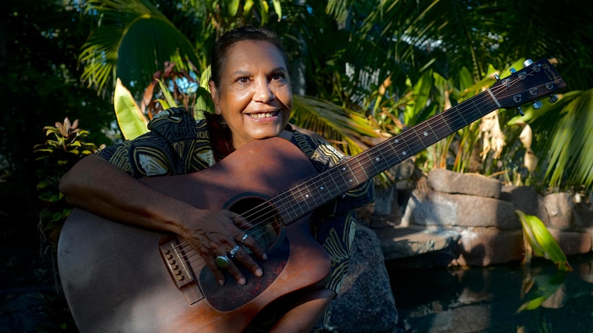 A woman holds an acoustic guitar.
