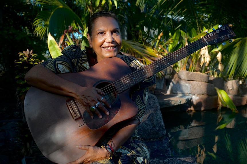 A woman holds an acoustic guitar.