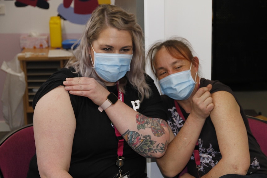 Two women in masks with sleeves rolled up after receiving a vaccine.