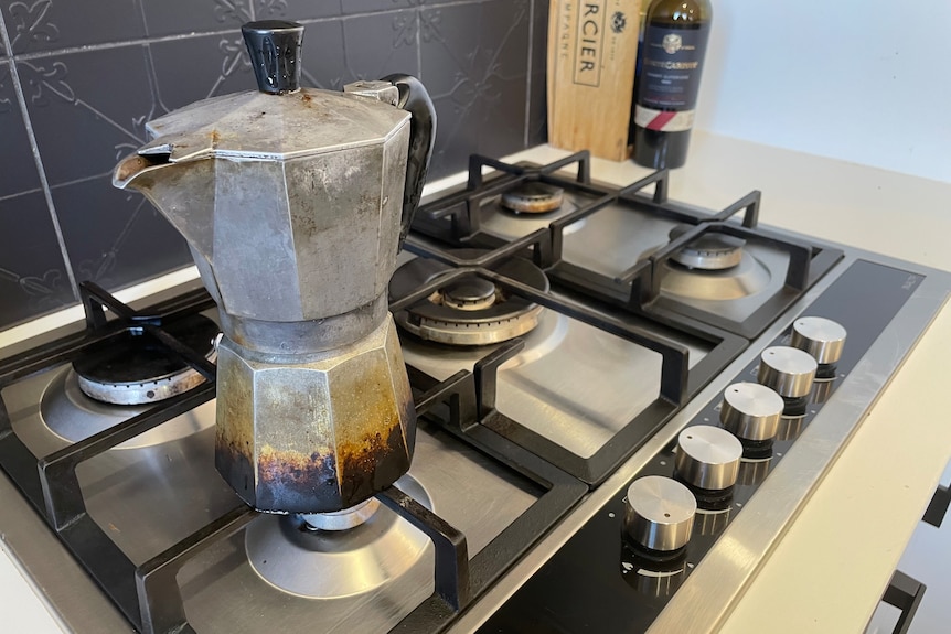 A coffee pot brewing on a gas stainless steel cooktop with a black patterned tile splashback