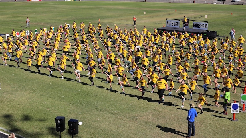 dancers in rows wearing yellow t-shirts dancing to Nutbush City Limits