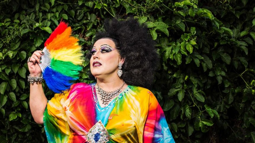 A man dressed as a woman (in drag) wearing a rainbow outfit