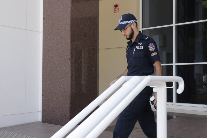 Photo of a male police officer with pale skin and a facial hair leaving court.