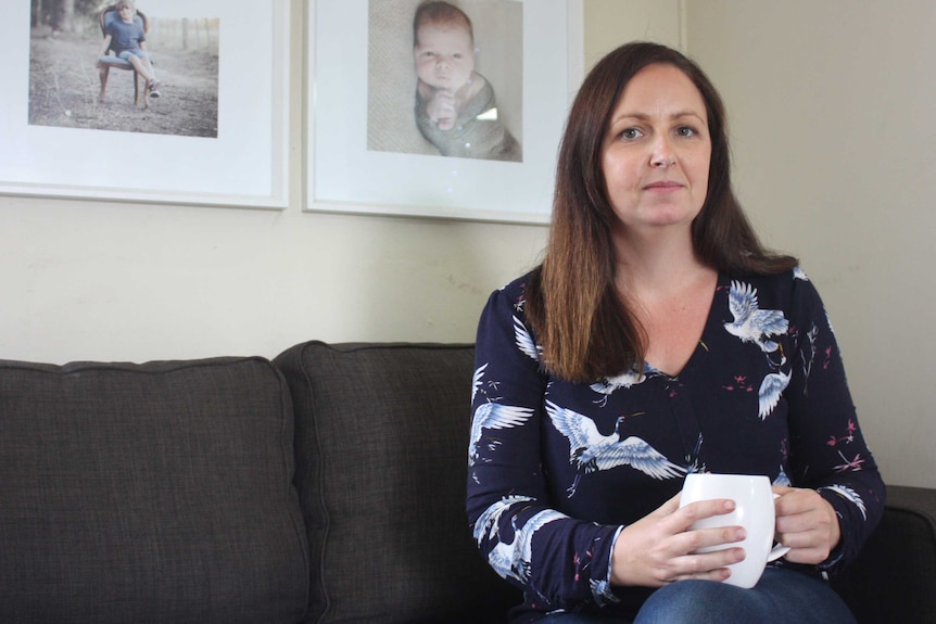 A woman sits on a couch, with photos of children hung on the wall behind her.