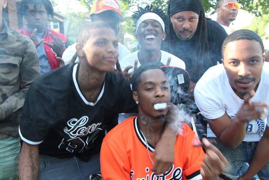 A group of African American men smoke, smile, gesticulate and pose for the camera.