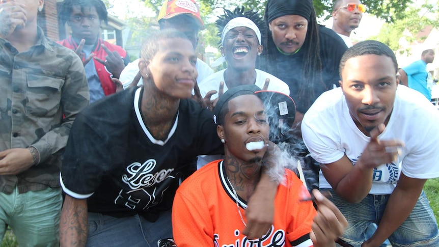A group of African American men smoke, smile, gesticulate and pose for the camera.