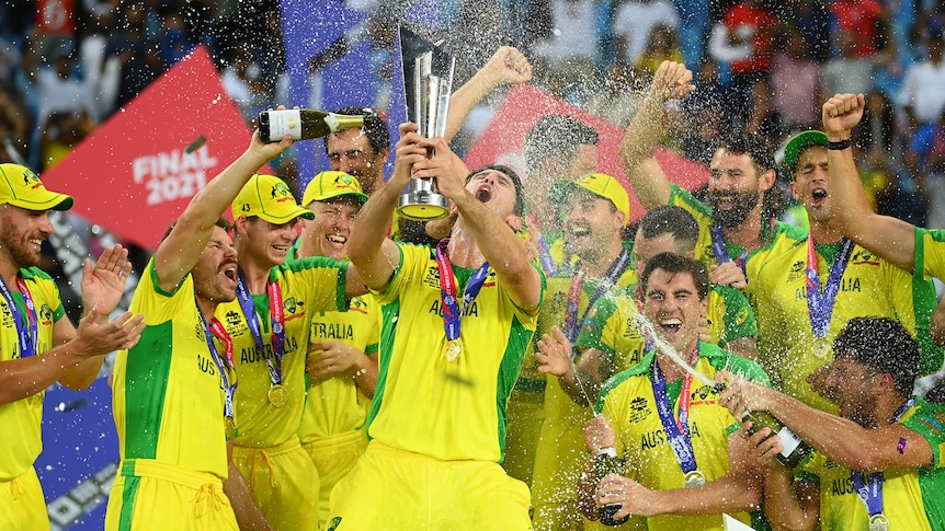 Australian players lift a trophy and spray champagne on a podium in celebration