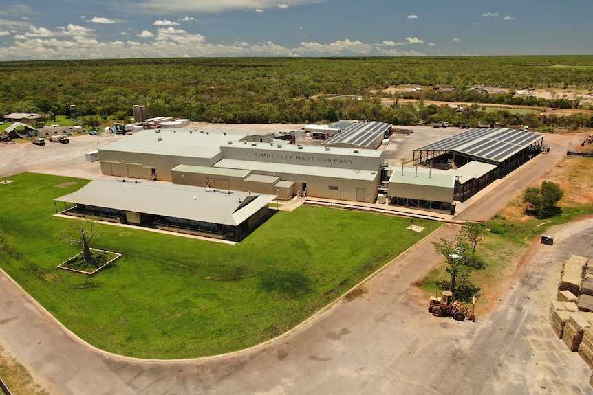 An aerial view of a factory surrounded by green trees and red dirt.