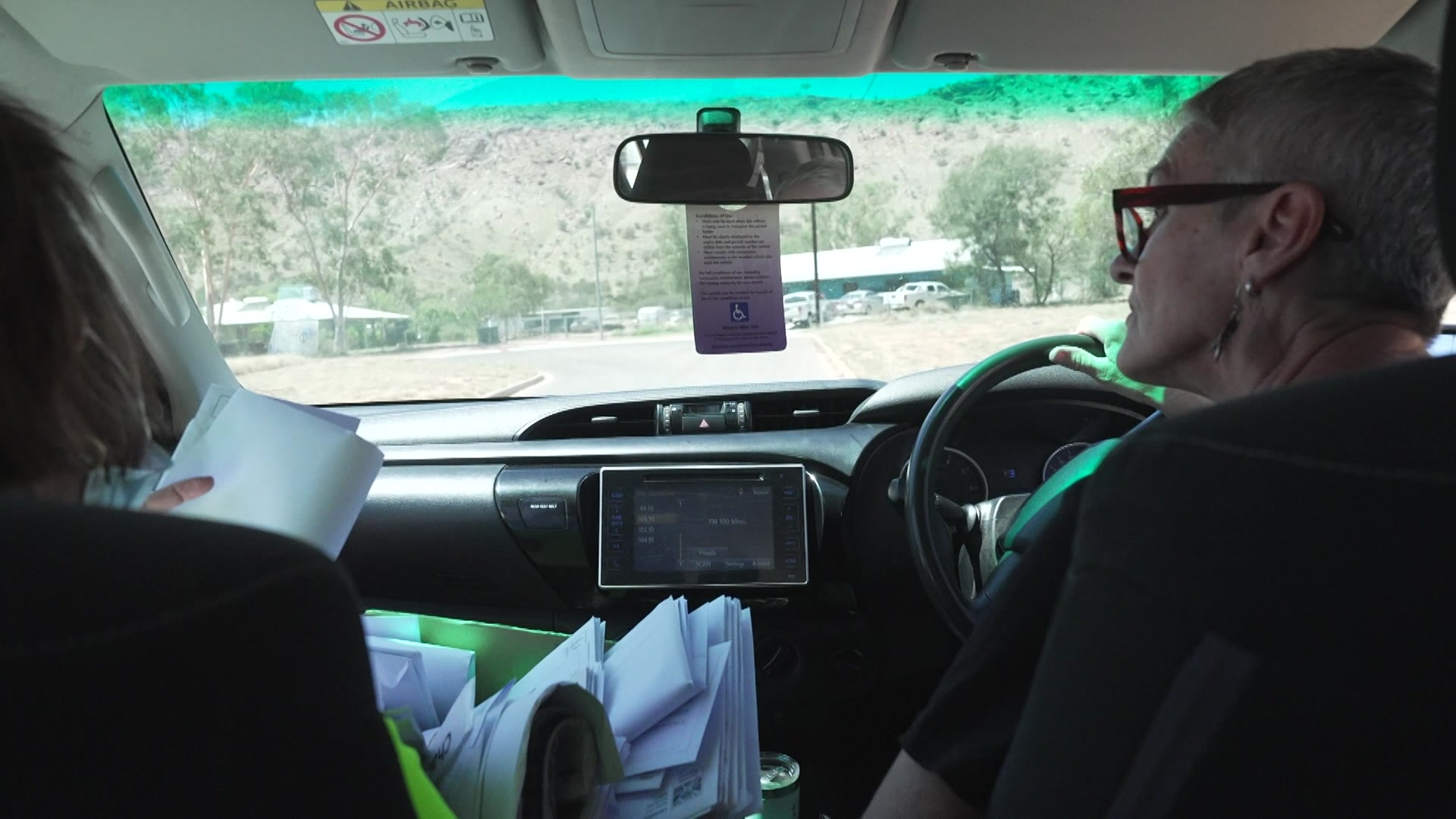 Duas mulheres no banco da frente de um carro entregando correspondência.