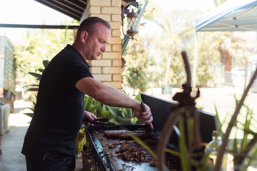 Colin Butland turns the sausages at a barbecue.