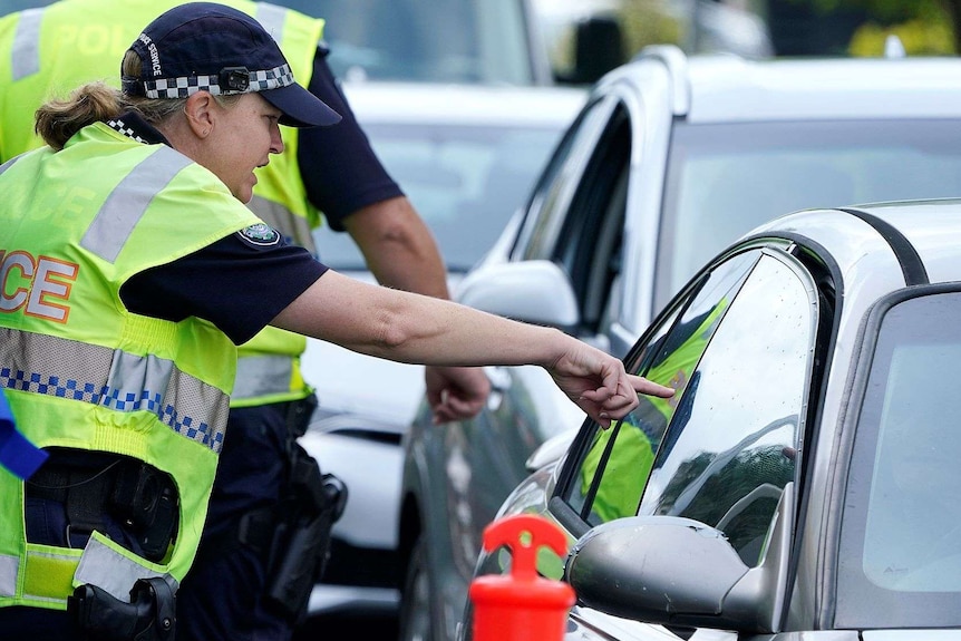 A police officer gestures to a driver in a car pointing at them