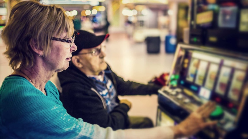 An older woman and man play a poker machine