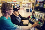 An older woman and man play a poker machine