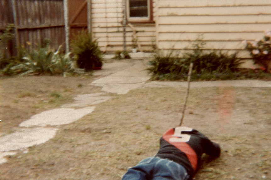 A young boy lies face down on the grass, with a number five clearly seen on the back of his jumper.