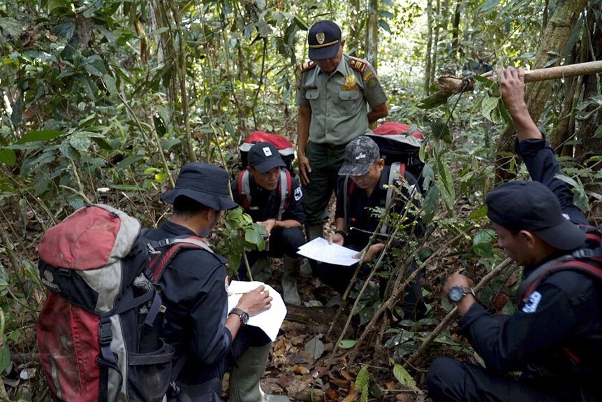 Four conservationists and an official kneel and check paperwork as they comb the dense jungle for animal traps.