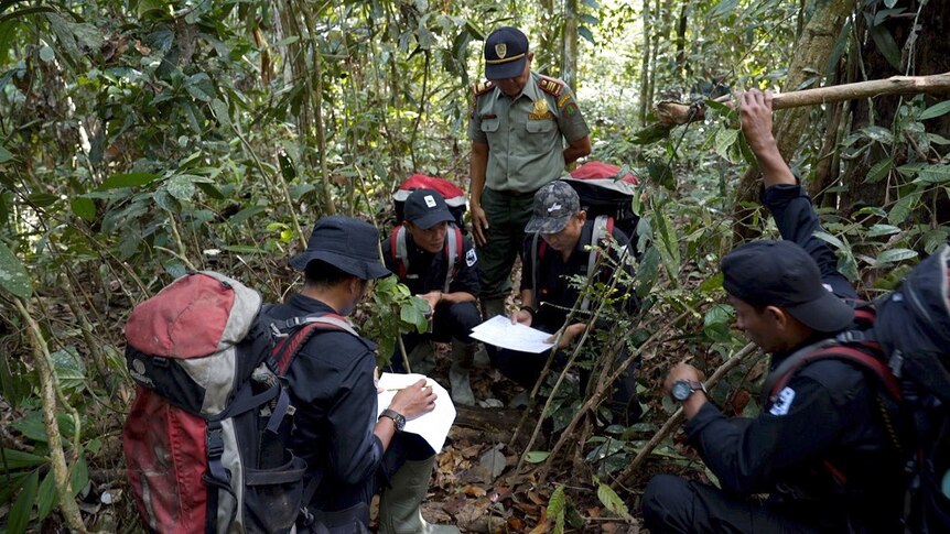 Four conservationists and an official kneel and check paperwork as they comb the dense jungle for animal traps.