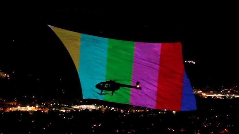 A helicopter flies alongside a big projection screen over New York