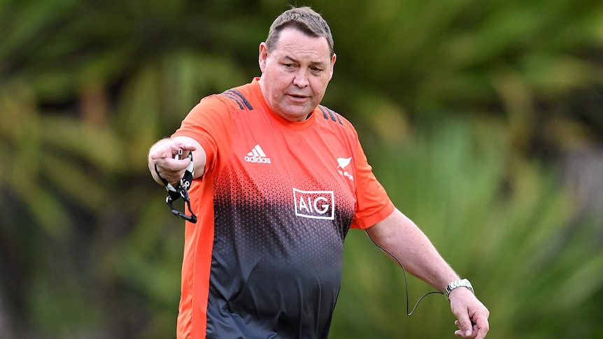 Steve Hansen, wearing an orange and black jersey, points his finger while walking