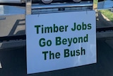 A freight truck is parked on the road on a sunny day with a sign attached to the front that says: Timber Jobs Go Beyond The Bush