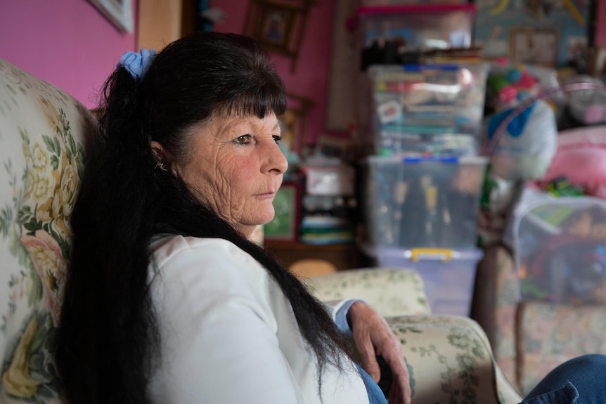 A middle aged woman sits on a couch in her home.