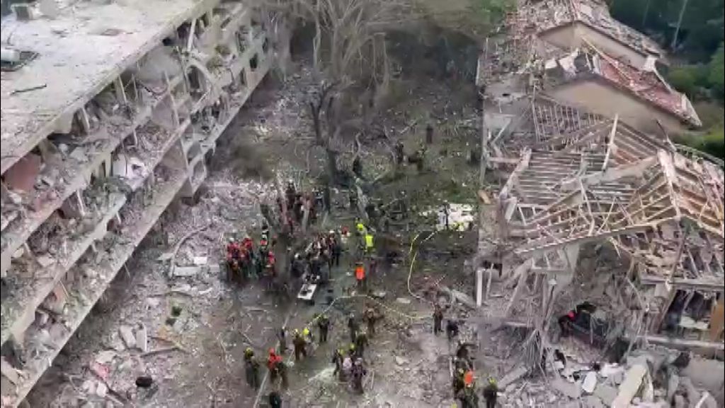 Drone shot of people in high vis amid rubble next to damaged buildings.