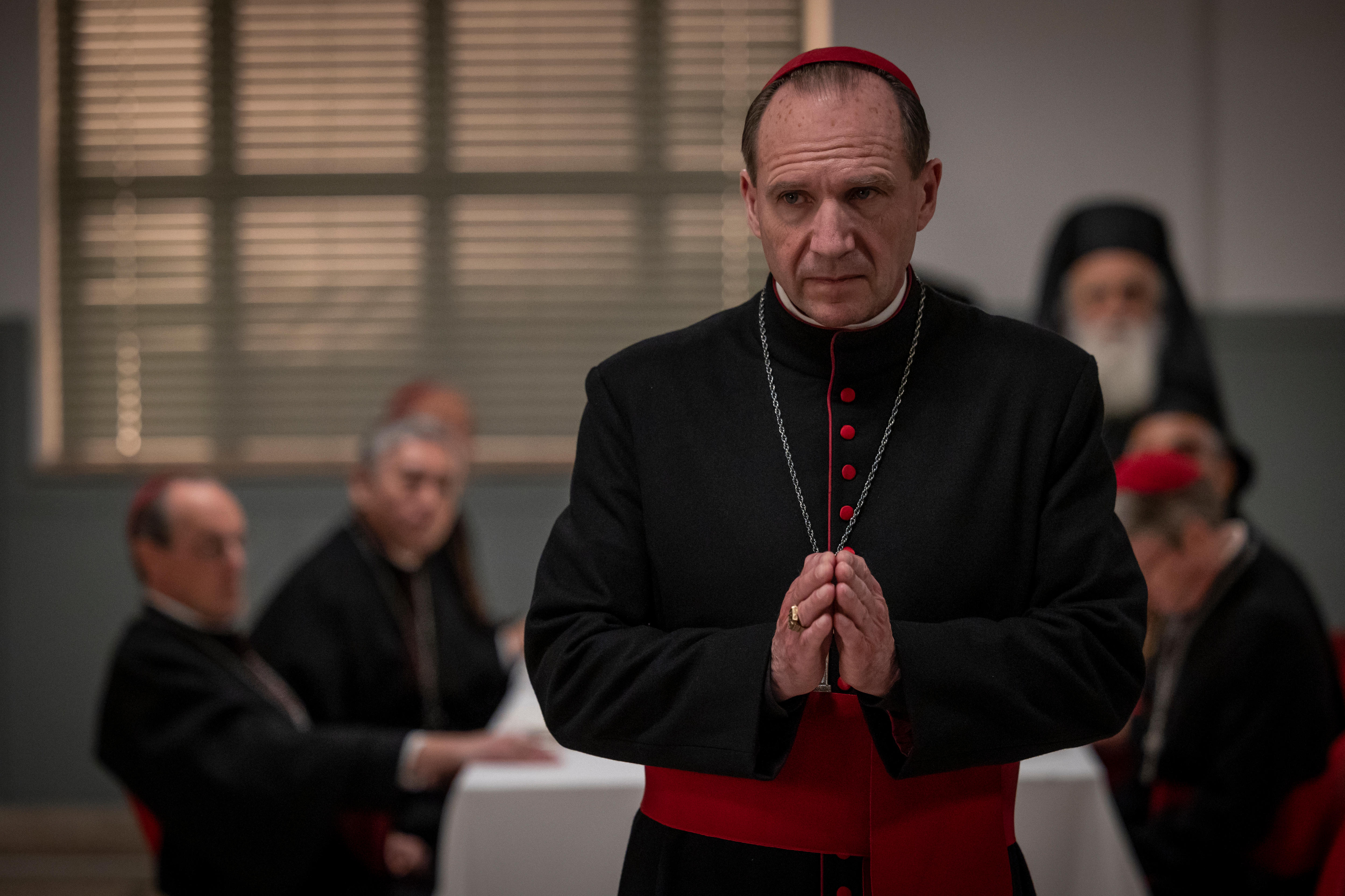 Ralph Fiennes puts his hands together in prayer in the dining room of the Conclave