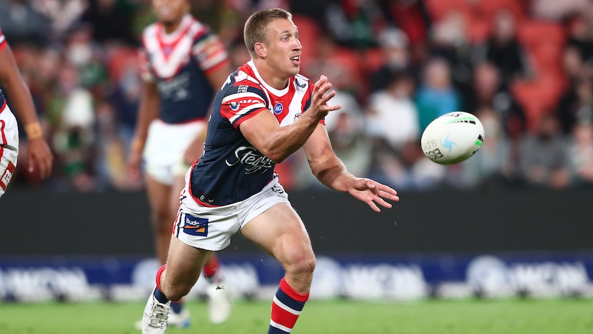 A Sydney Roosters NRL player passes the ball to his left against the Rabbitohs.