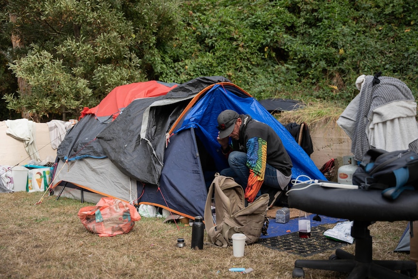 A man kneels in front of a tent putting things in a small backpack. 