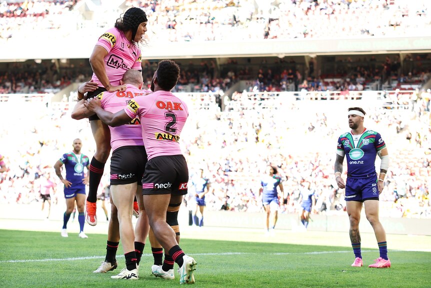 Jarome Luai jumps on Penrith Panthers teammates after a try in an NRL game against the Warriors.