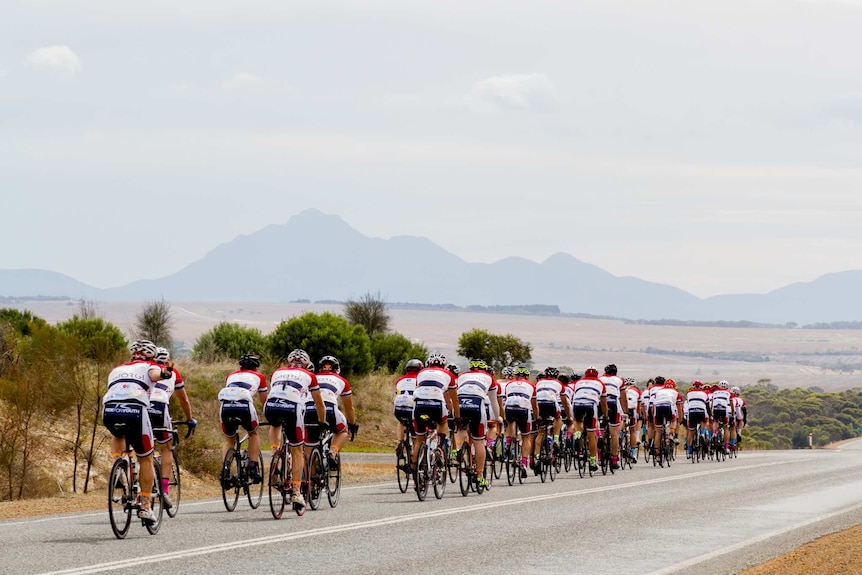 A group of cyclists riding on a road with a mountain range in the background