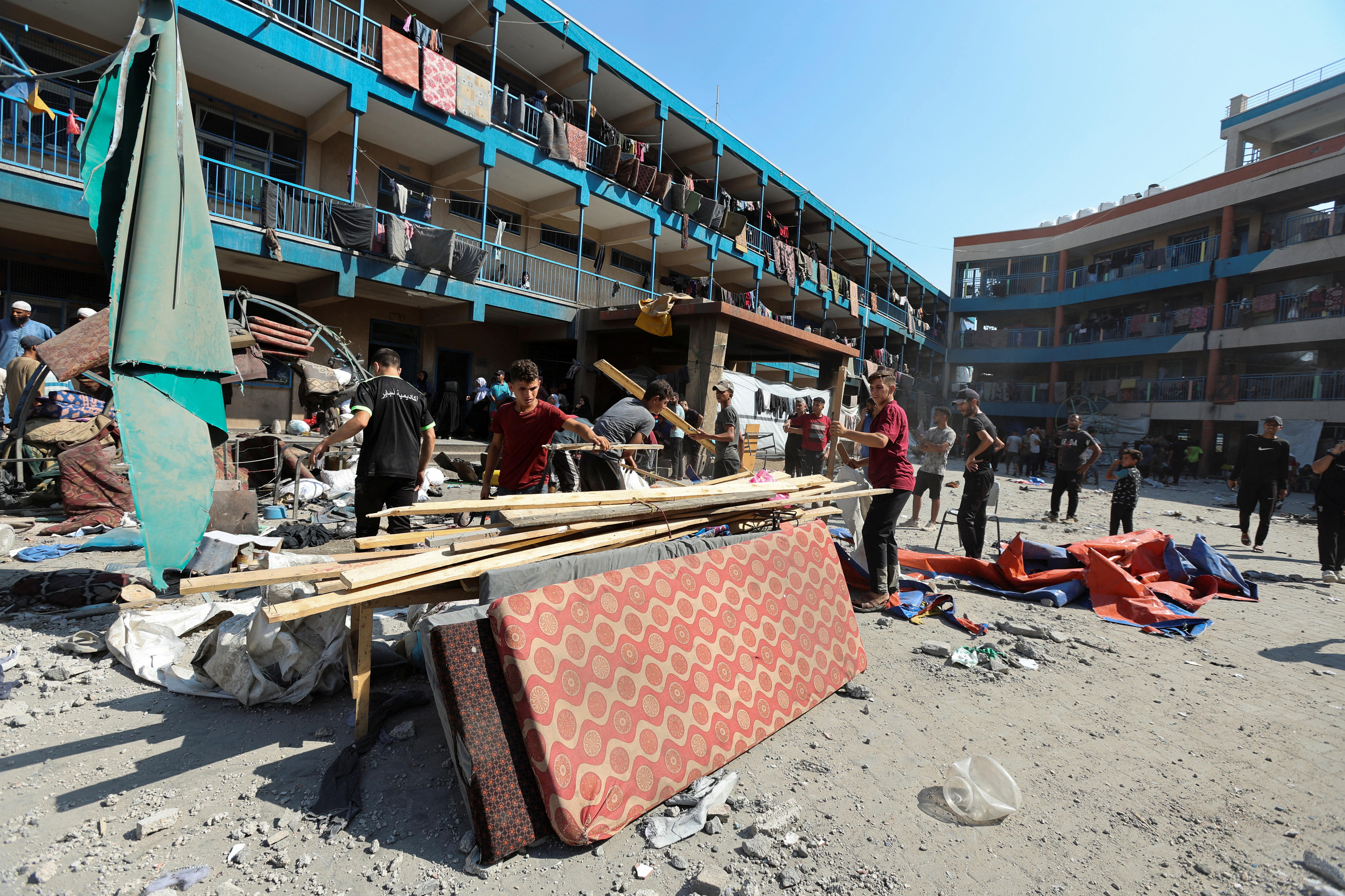 People stand in the courtyard of a large building complex with wood pilled up on top of mattresses