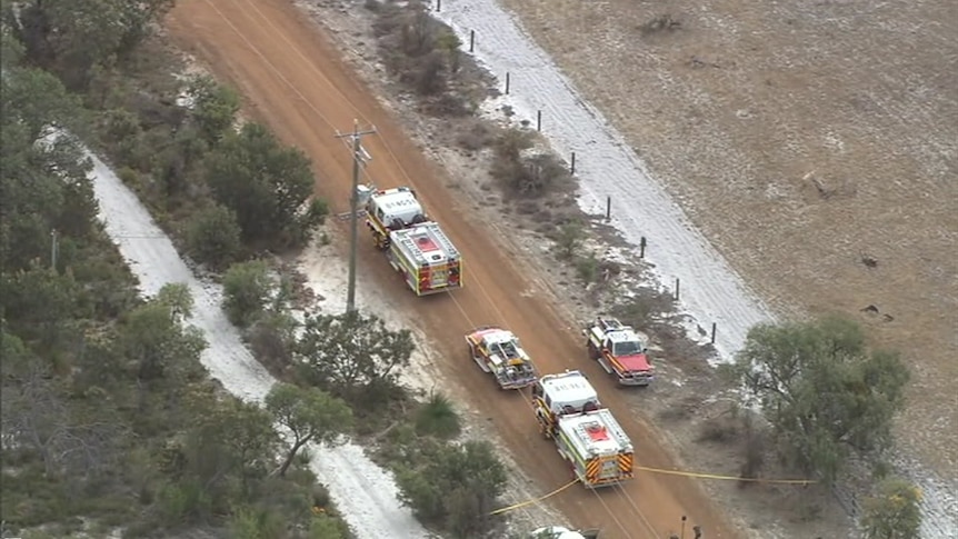 Four emergency services vehicles are parked along a dirt road in a rural area.