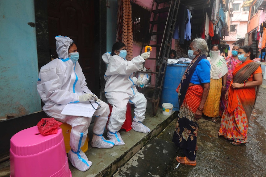 Two people in full medical PPE suits scan a line of women with a temperature gun.