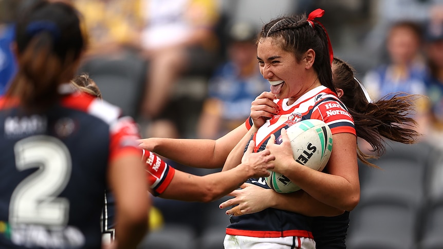 Olivia Kernick sticks her tongue out as she's hugged by teammates while celebrating a try for the Roosters.