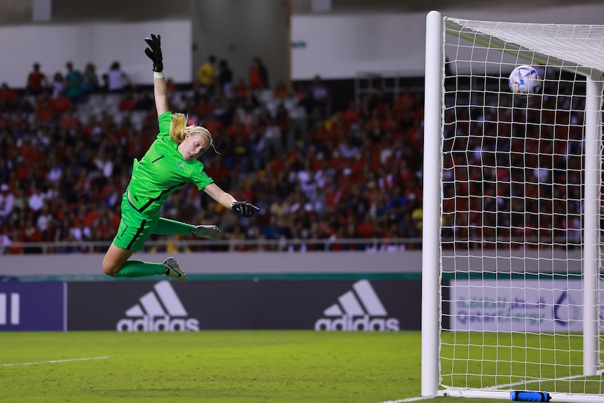 A female goalkeeper dives to try and stop a goal