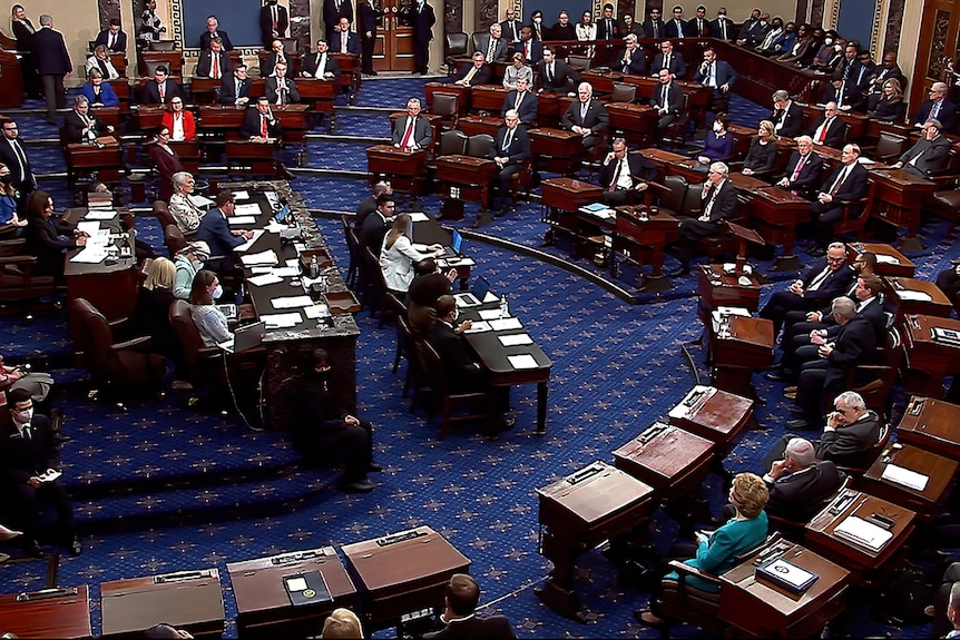 The US senate are seen in session sitting at a circle of desks.