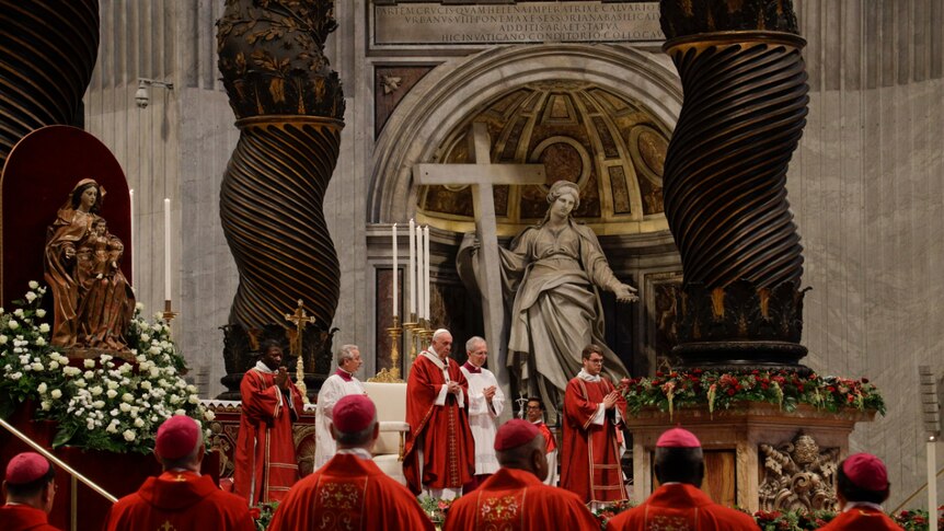 You look to the ornate altar of St Peter's Basilica behind a row of cardinals draped in red vestments and pink skull caps.