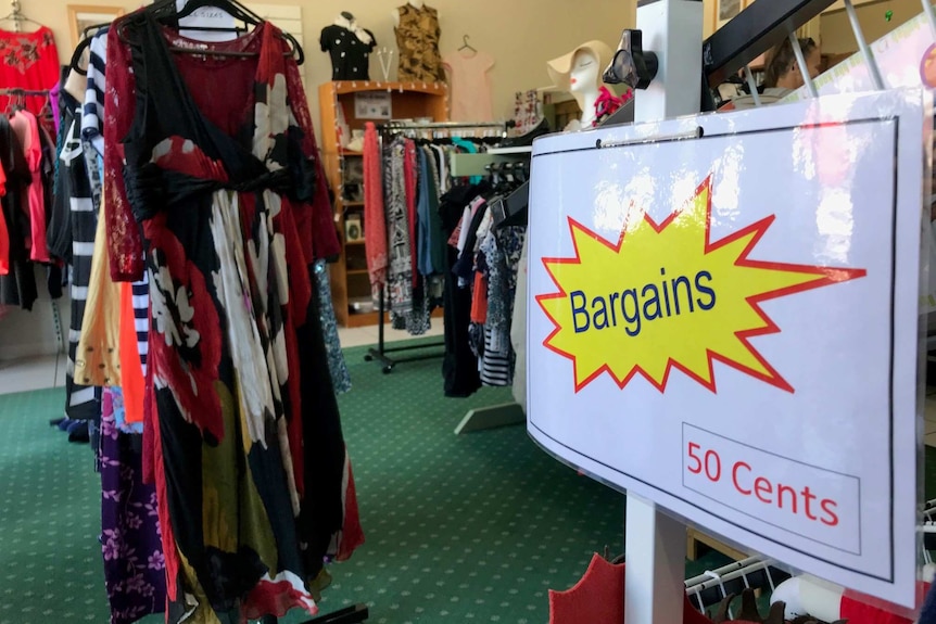 A laminated bargain sign in front of racks of second-hand clothes.